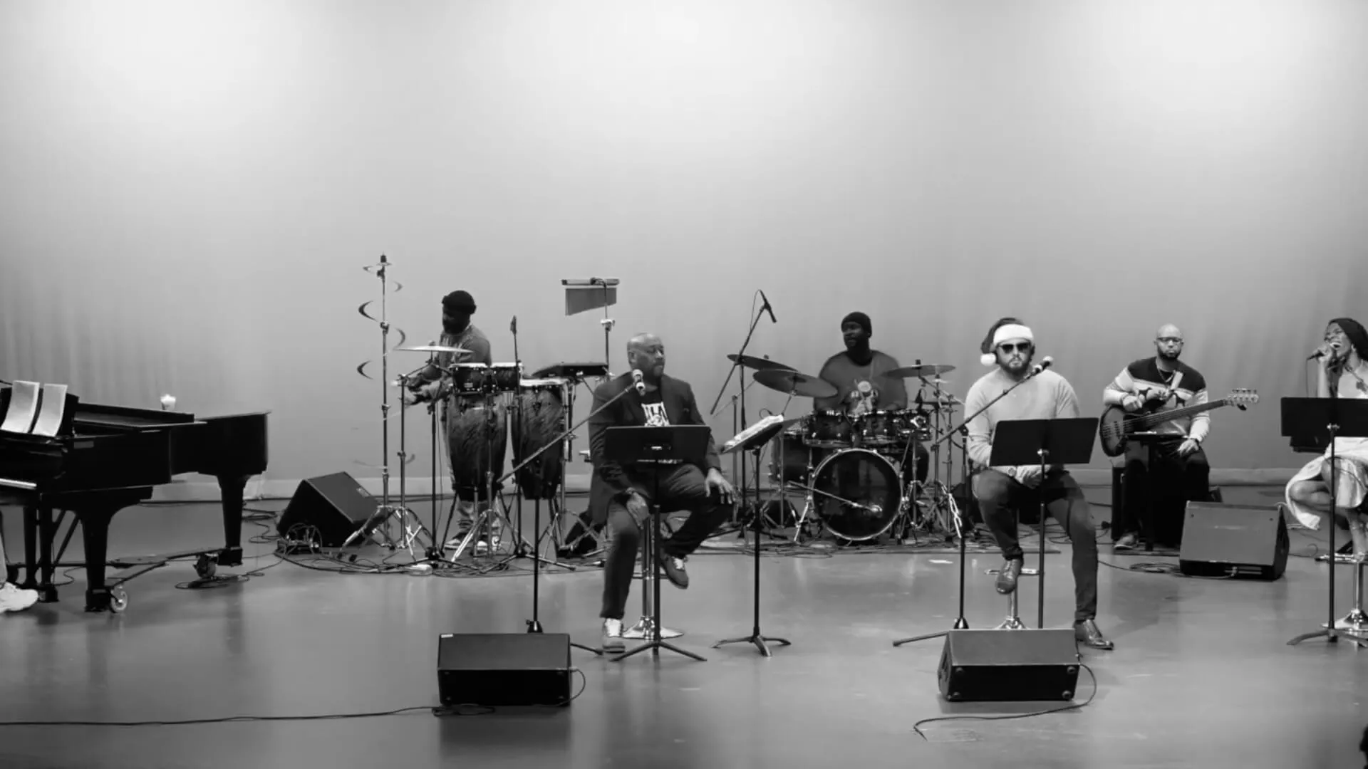 A jazz ensemble performs on stage in a black-and-white photograph, with piano, drums, and horns.